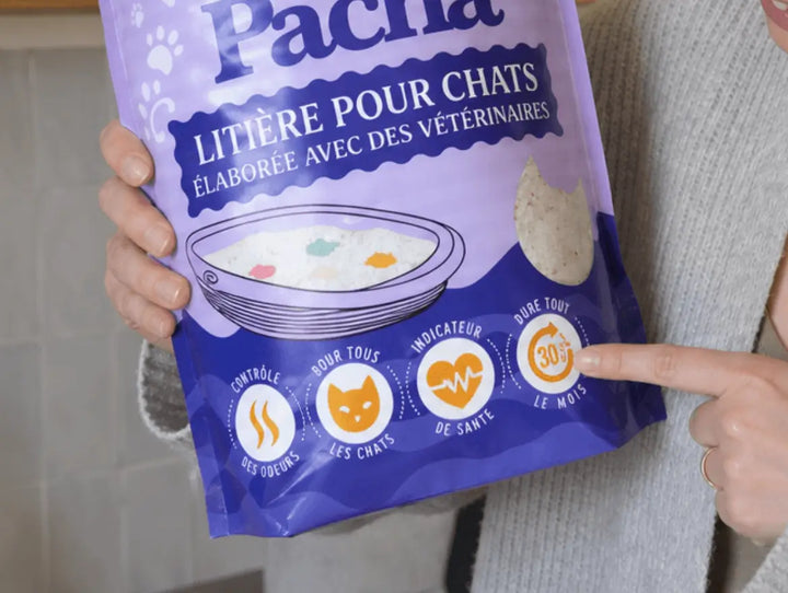 Gros plan sur le sac Pacha violet — doigt qui pointe le pictogramme « Dure tout le mois — 30 jours » à côté des icônes contrôle des odeurs, pour tous les chats, indicateur de santé
